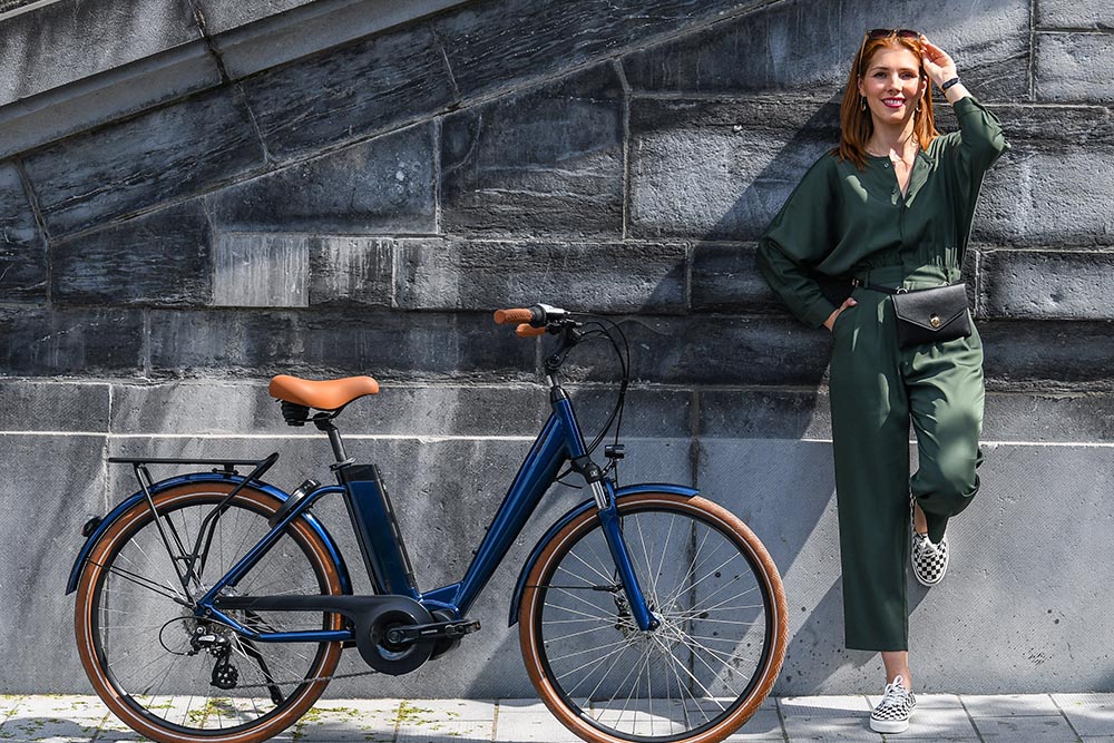 Une femme adossée à un mur à côté de son vélo électrique